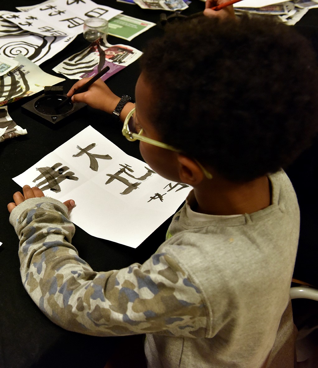 Atelier jeune public, enfant entrain d'écrire à l'encre chinoise 